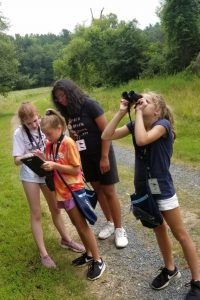 A group of children stand on the Kellogg Bird Sanctuary's Lake Loop Trail, using binoculars and a tablet computer to study birds.