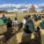 MSU President Kevin Guskiewicz speaks to the group from the inaugural Spartan Bus Tour, who are sitting on straw bales in the foreground, at the KBS Long-term Agroecosystem Research site.