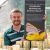 David Pavlik poses in a greenhouse at John Ball Zoo with an informational placard on his research project with Poweshiek skipperlings.