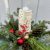 A holiday arrangement featuring evergreen boughs, pine cones and tree ornaments with a birch bark candle in the center.